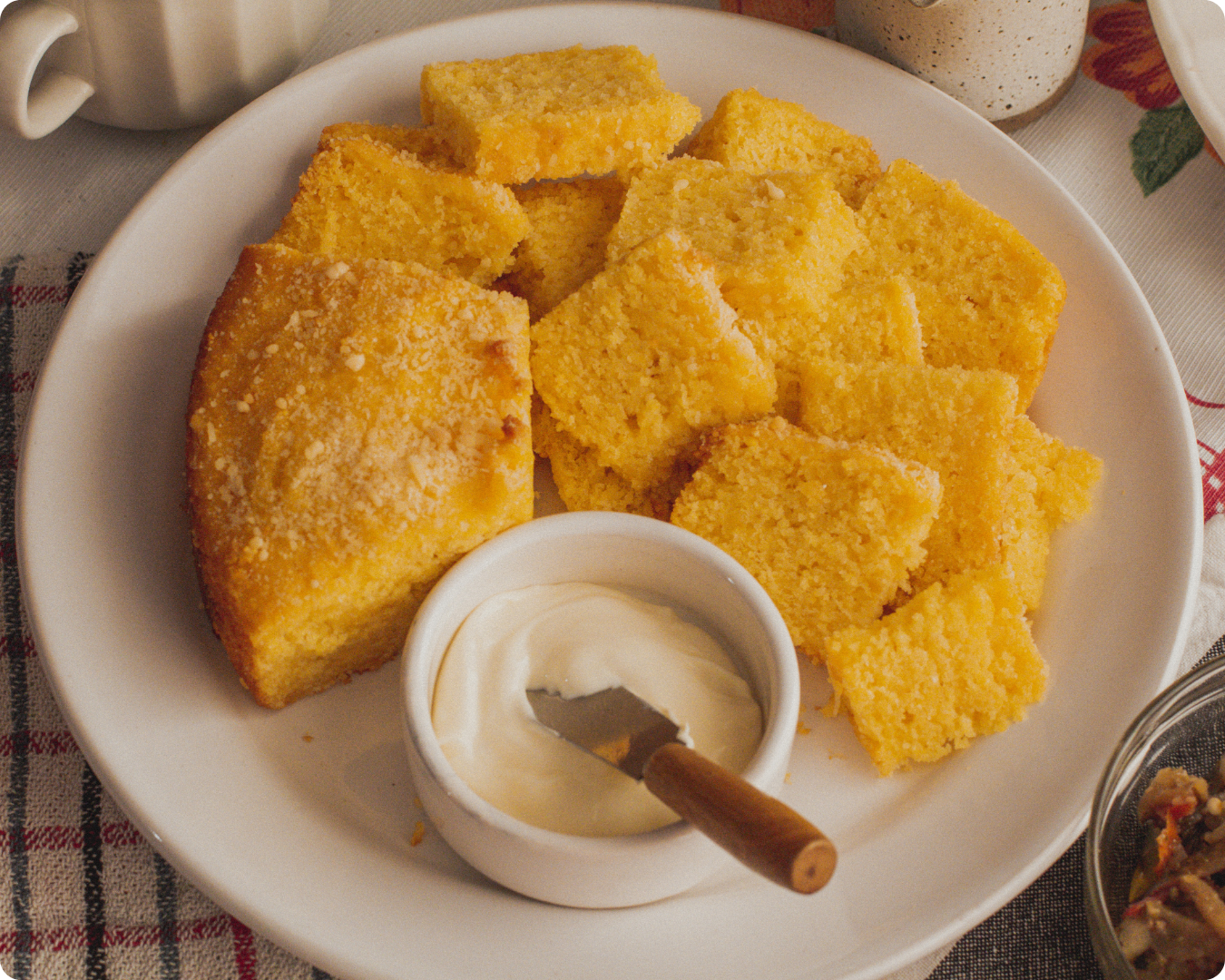 um prato com diversos pedaços de bolo de fubá dispostos lado a lado e também sobrepostos, servidos com um potinho com requeijão, que combina muito com a receita de bolo de fubá