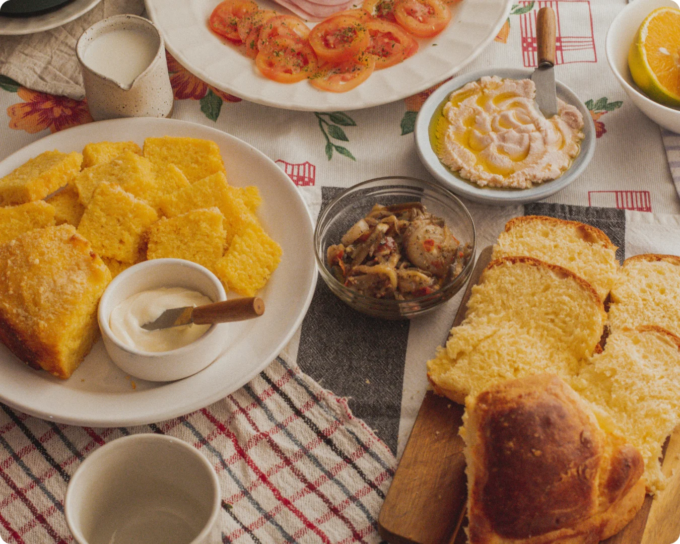 mesa posta com bolo de fubá que é a receita em questão, pão brioche, caponata de berinjela e outros elementos que compõem uma mesa de café da tarde
